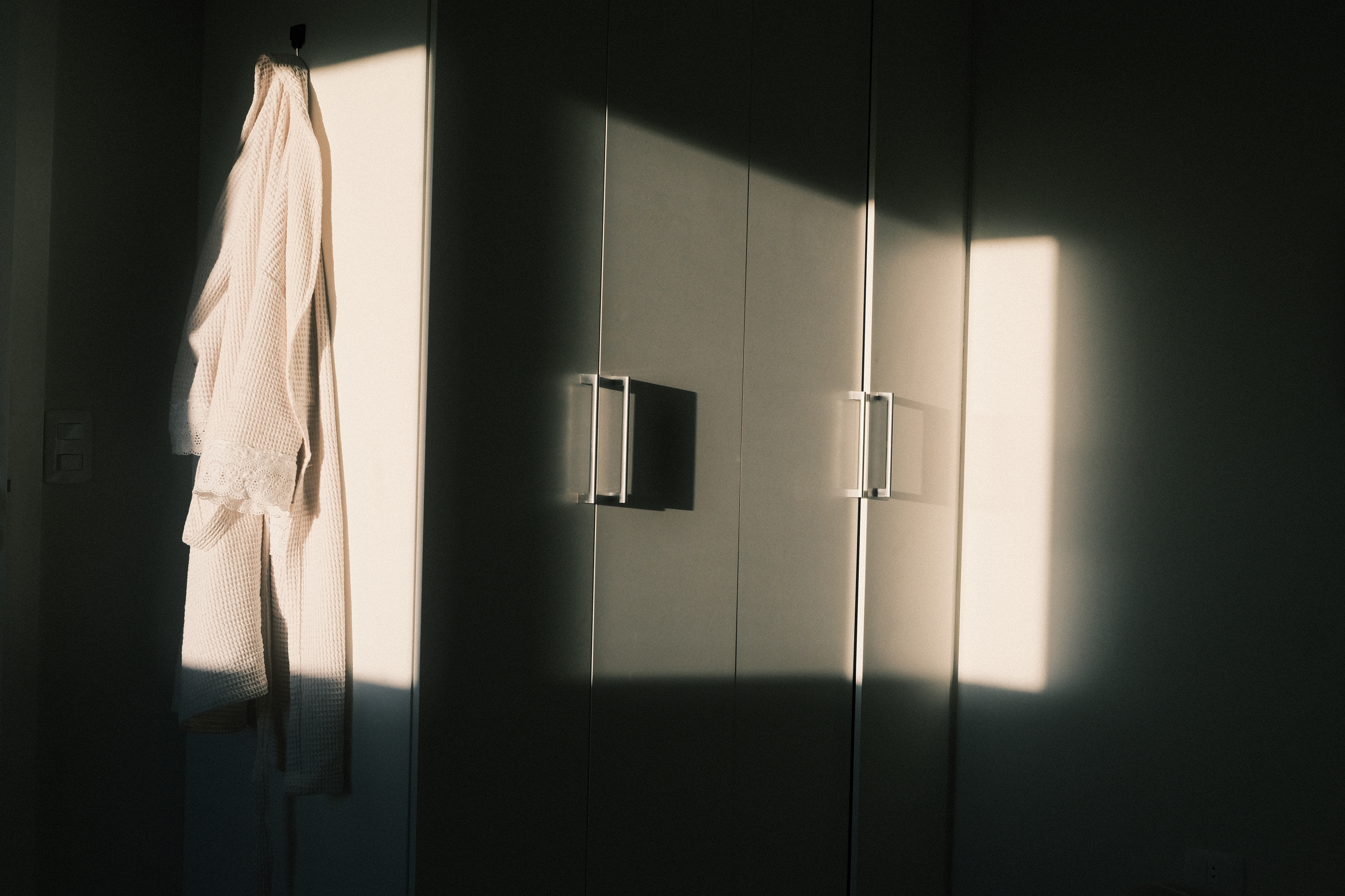 Taken from my bed, a photo of my girlfriend's cupboard with her bathrobe hanged on the side, a stream of sunlight comes in such a way that makes a frame of light in the middle of the image